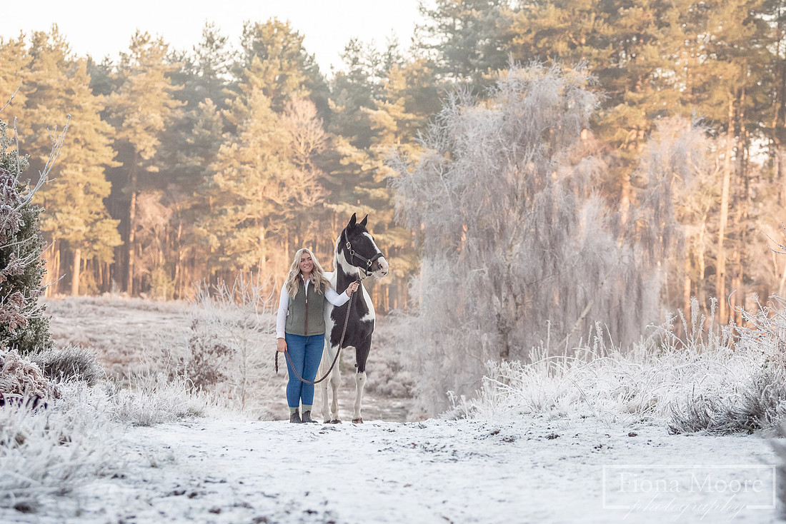Portait of a woman and skewbald mare in a snowy landscape taken at Cannock Chase. Photograph taken by West Midlands Based Specialist Equine Photographer Fiona Moore Photography